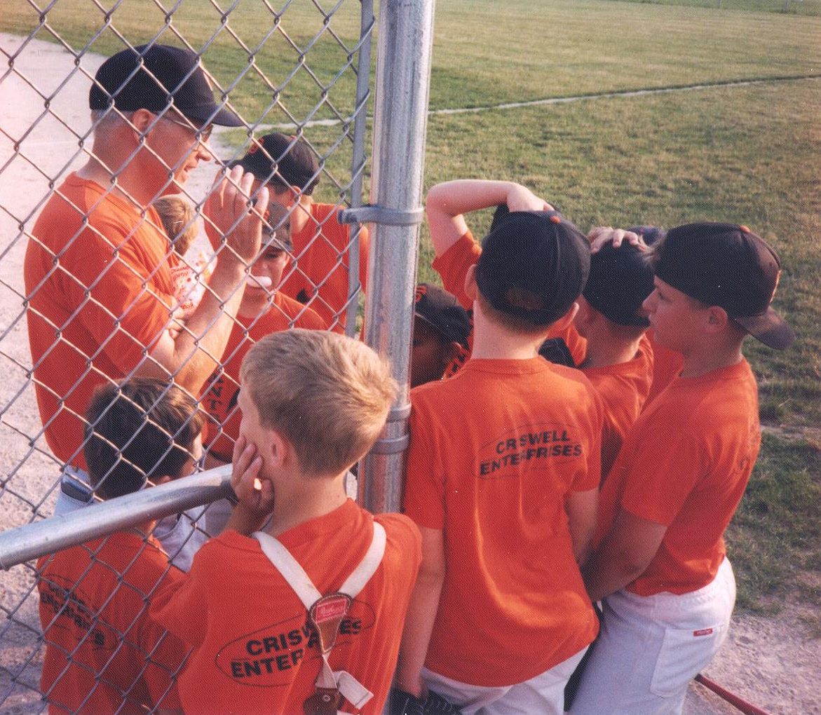 David Brandt, coaching little league. son Josiah (the hatless catcher) and his teammates listen to a pep-talk. Photo courtesy of Bridget Brandt
