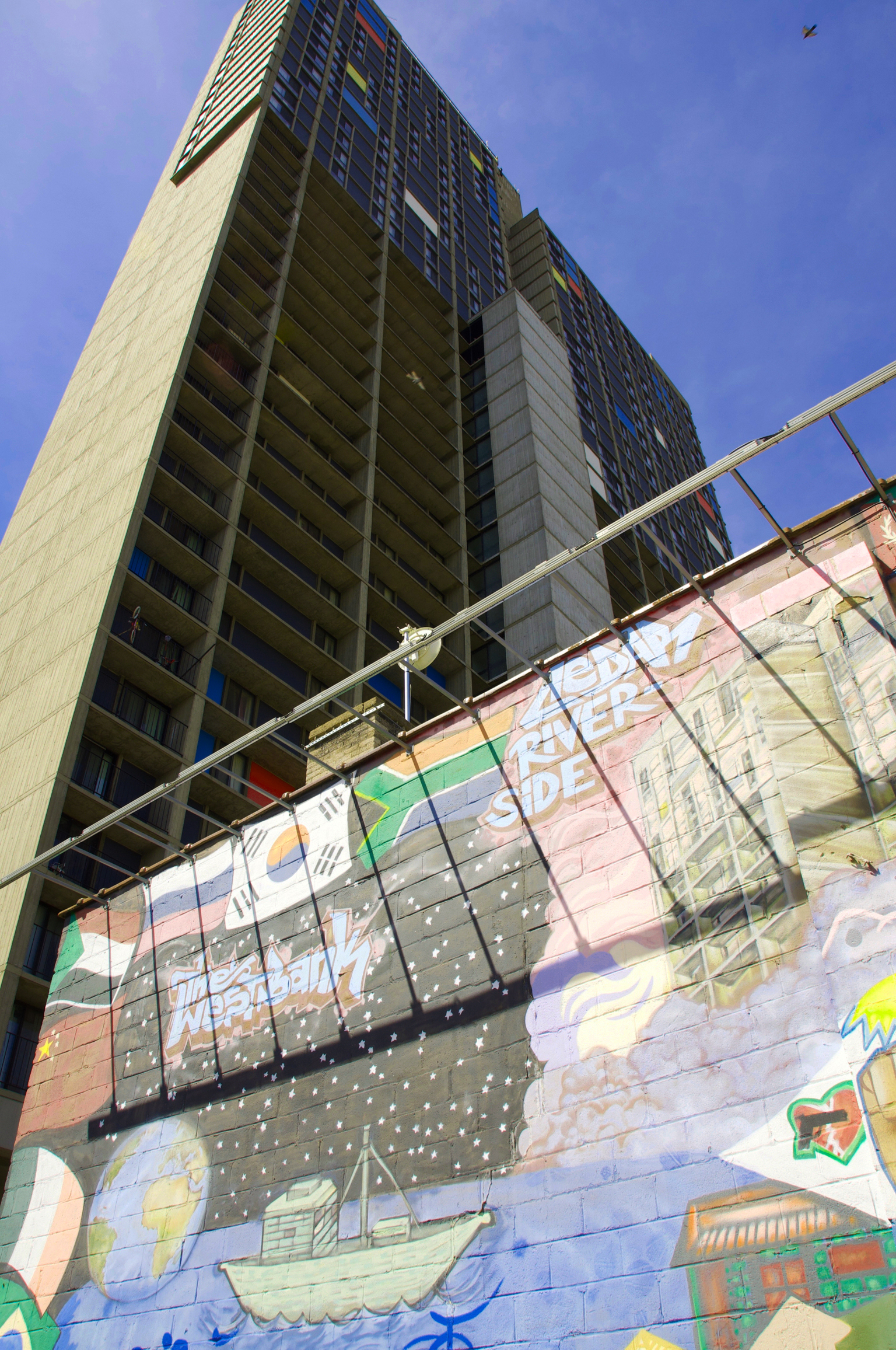 One of several high-rise apartment buildings Cedar-Riverside that is home to a large part of Minneapolis's Somali population. The wall mural in the foreground, with its many flags and depictions of various cultural elements, highlights the area's diversity